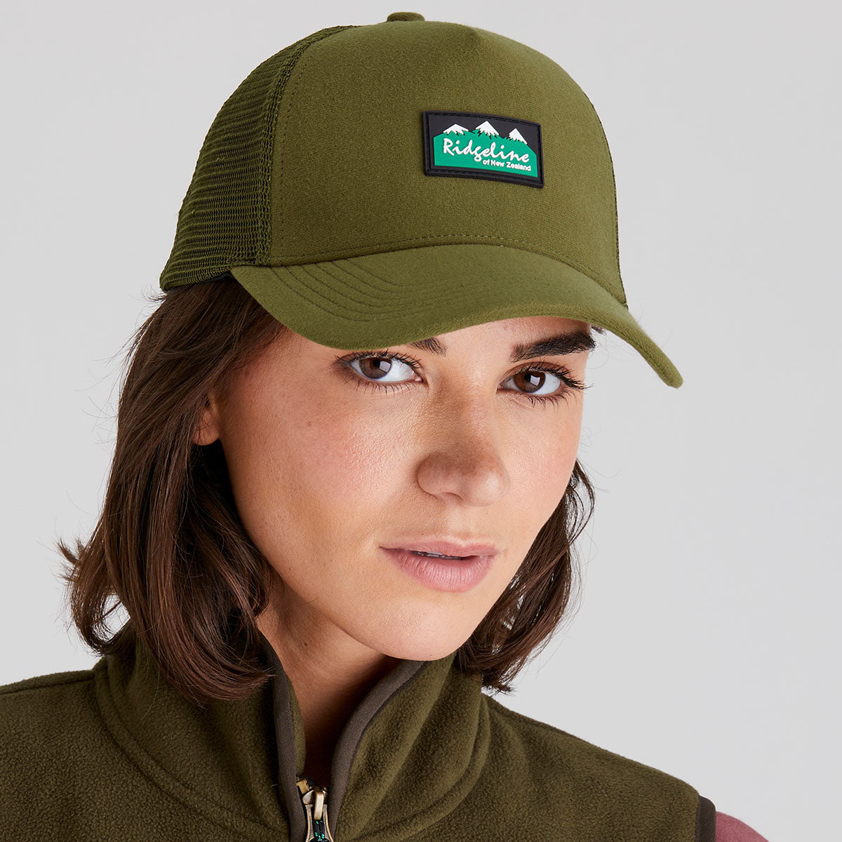 woman wearing a green cap with a visible brand logo against a plain background