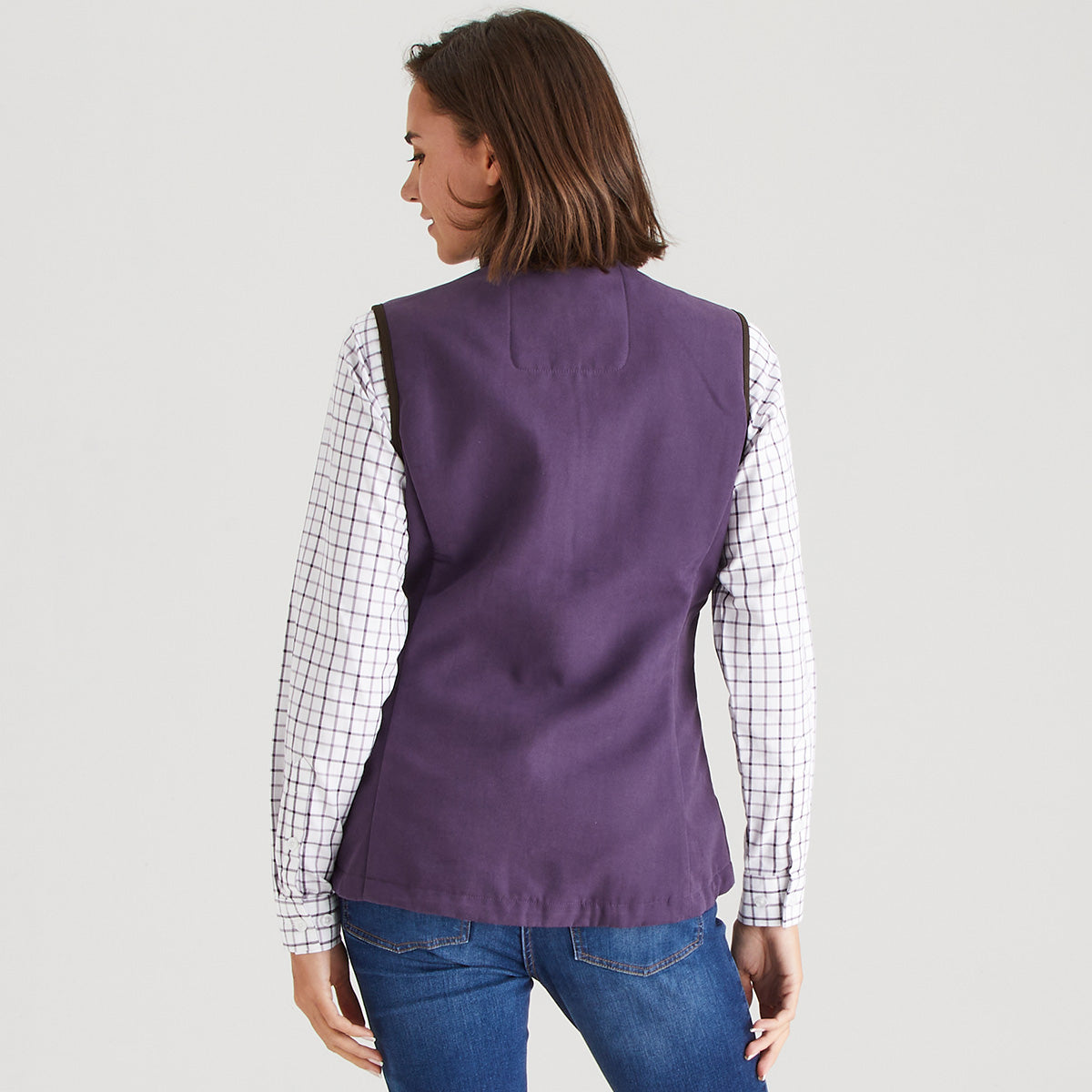 Person wearing a purple vest over a checkered shirt on a plain background