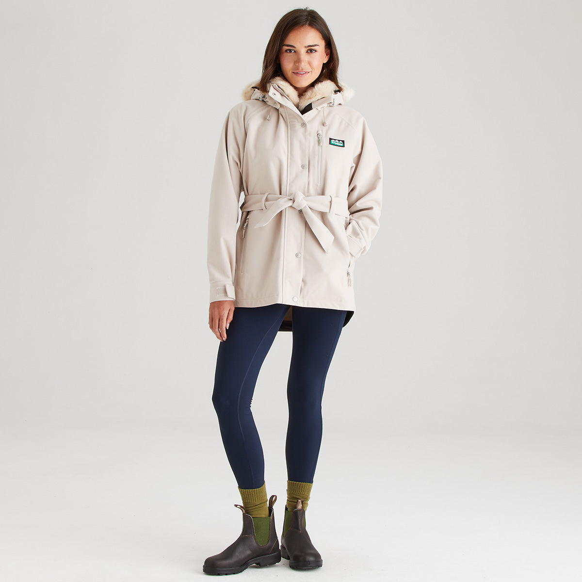 Woman wearing a cream raincoat with a brand logo on a white background