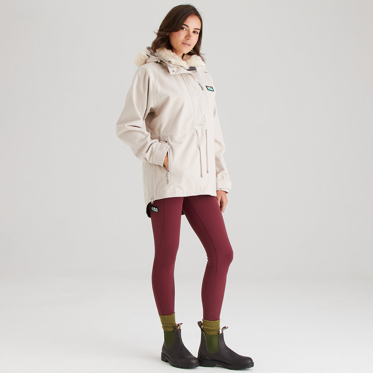 Woman wearing a cream raincoat, maroon leggings, and green socks on a white background