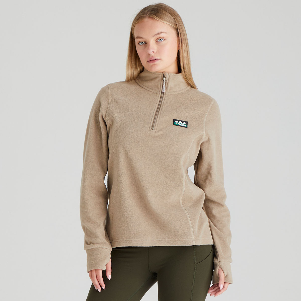 Woman wearing a beige pullover with a brand logo on a light grey background