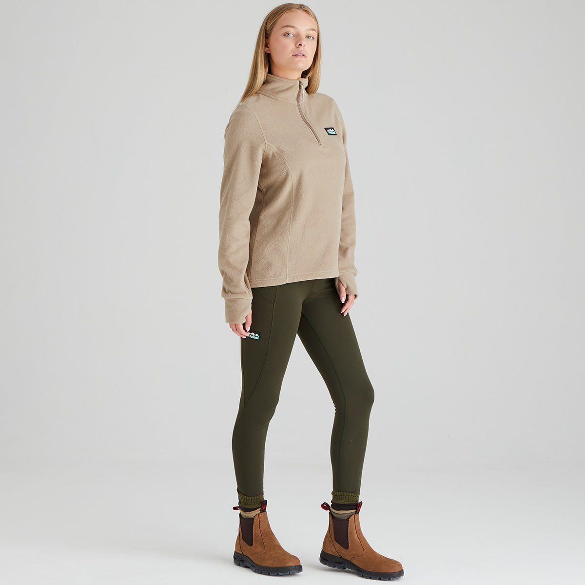 Women wearing a beige pullover, green leggings, and brown boots on a white background