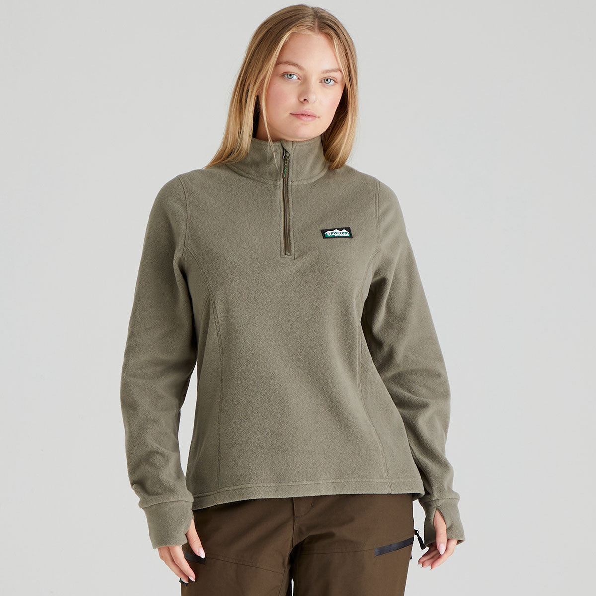 Woman wearing a green pullover with a small logo on a light grey background