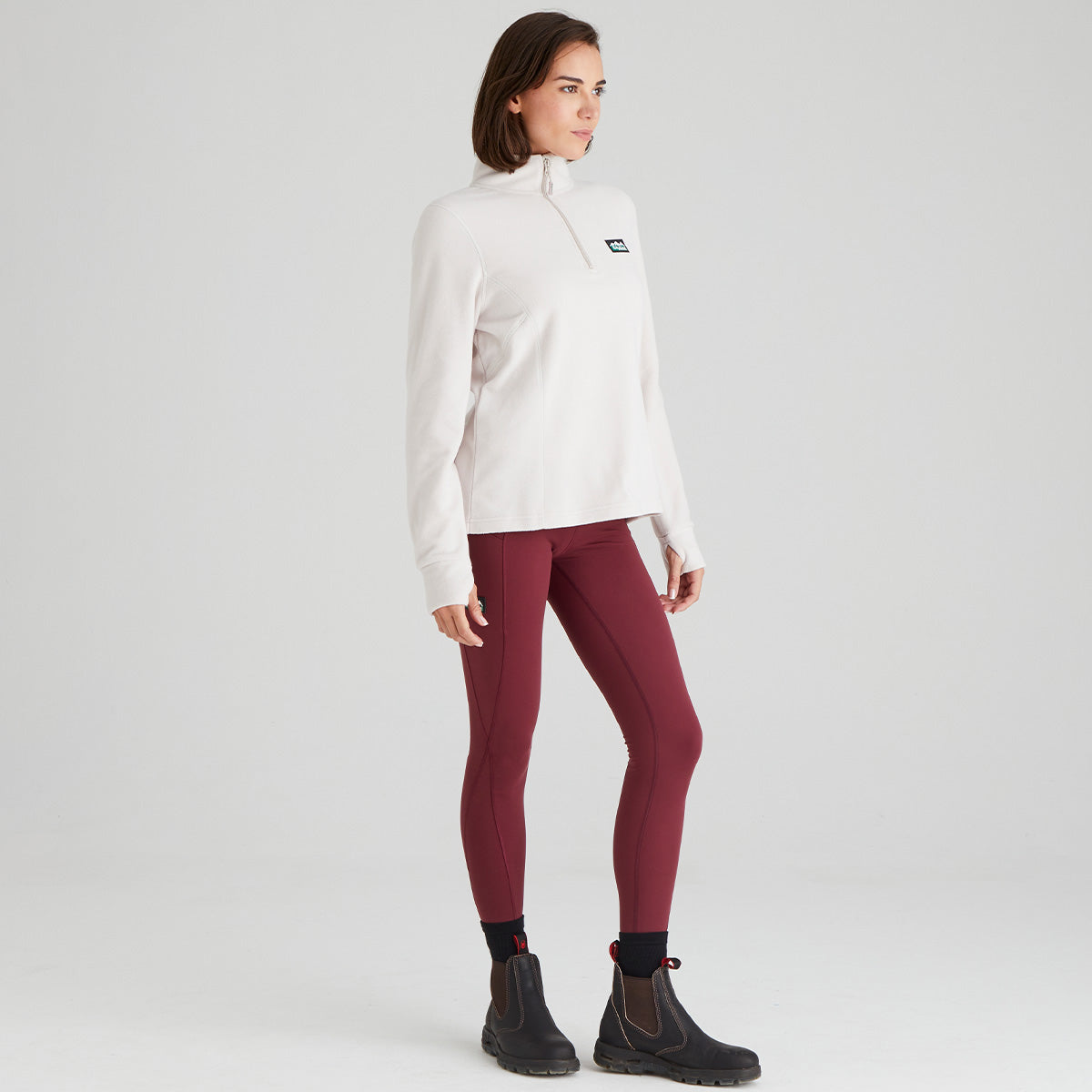 Woman wearing a white high-necked top and maroon leggings on a light grey background