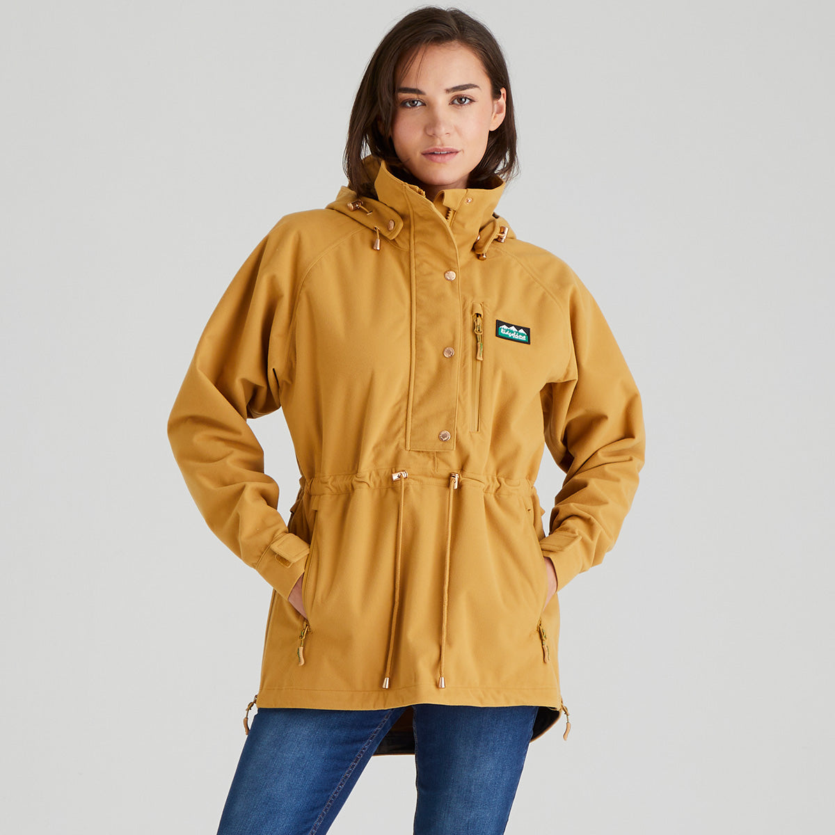 Person wearing a mustard yellow raincoat with a brand logo on a gray background