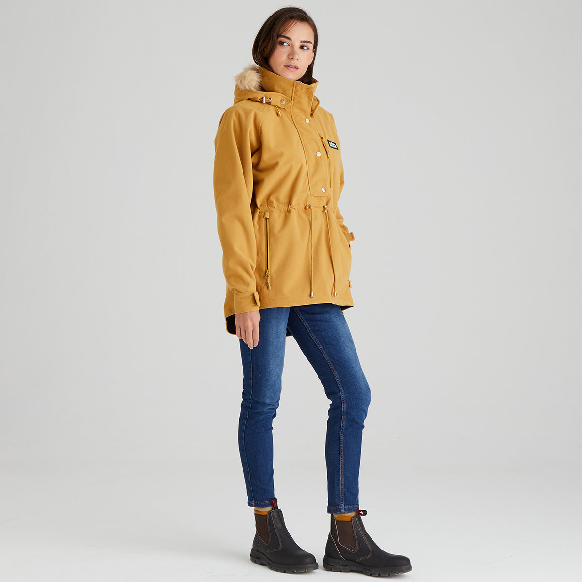 Woman wearing a mustard yellow parka with fur hood on a white background