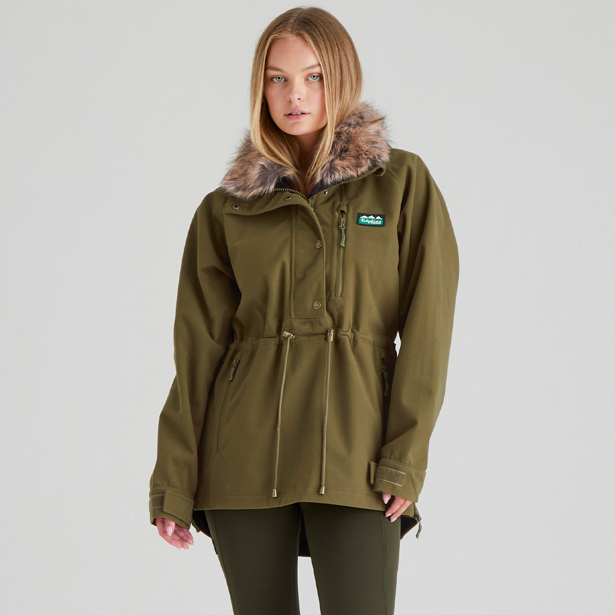 Woman wearing a green jacket with fur hood on a grey background