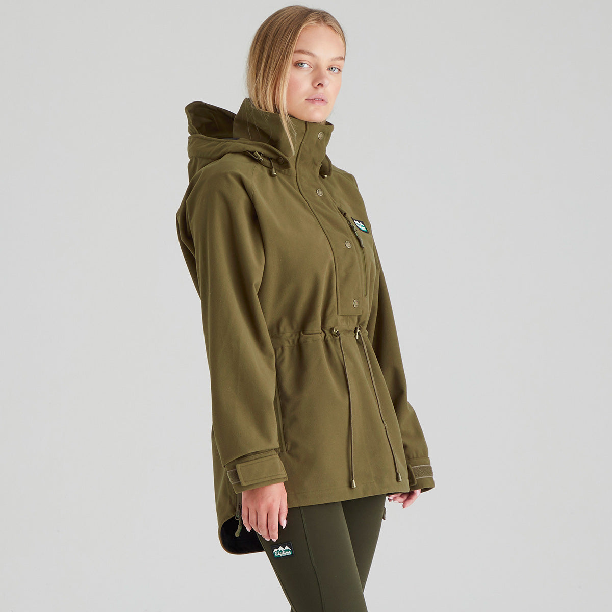 Woman wearing a green parka jacket on a grey background