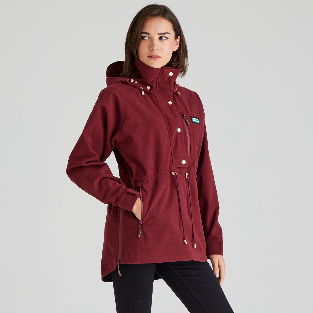 Woman wearing a maroon jacket with a brand logo on a grey background