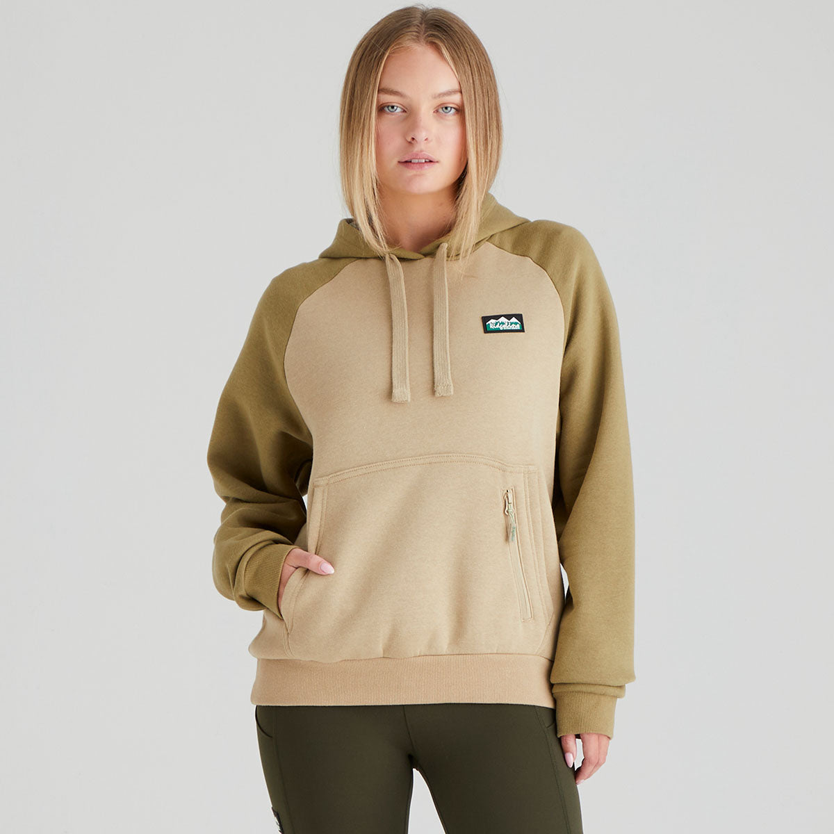 Person wearing a beige and brown hoodie with a logo on a grey background