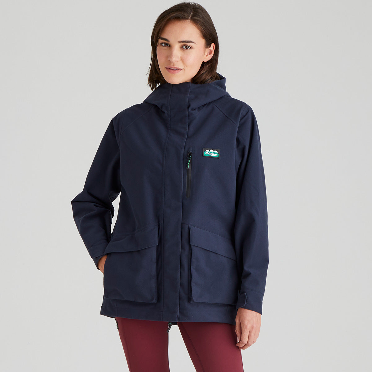 Woman wearing a navy blue jacket with a brand logo on a grey background
