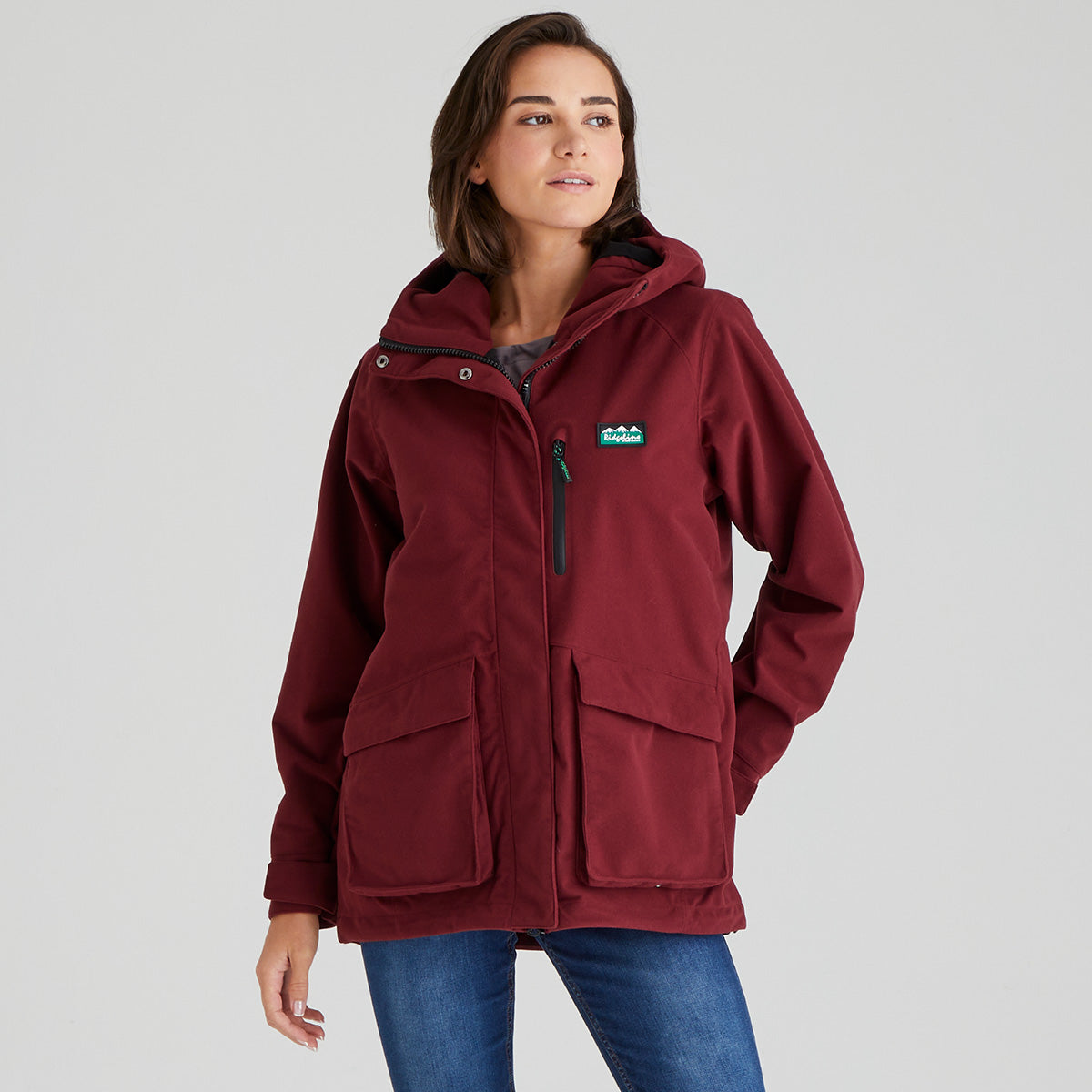 Woman wearing a maroon jacket with a brand logo on a grey background
