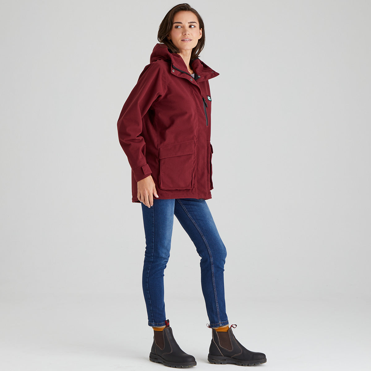 Woman wearing a red jacket and blue jeans on a light grey background