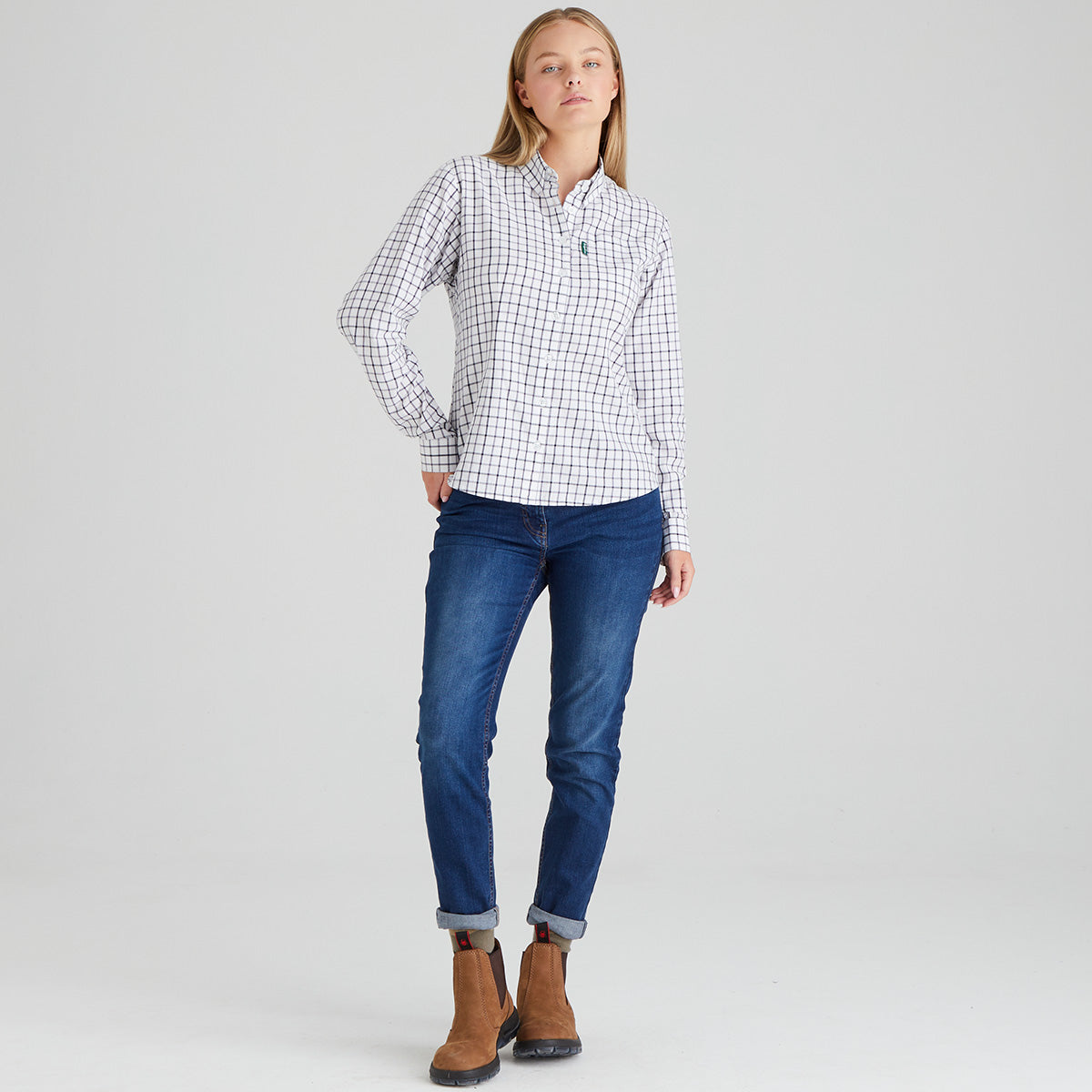 Woman wearing a checkered shirt, blue jeans, and brown boots on a grey background