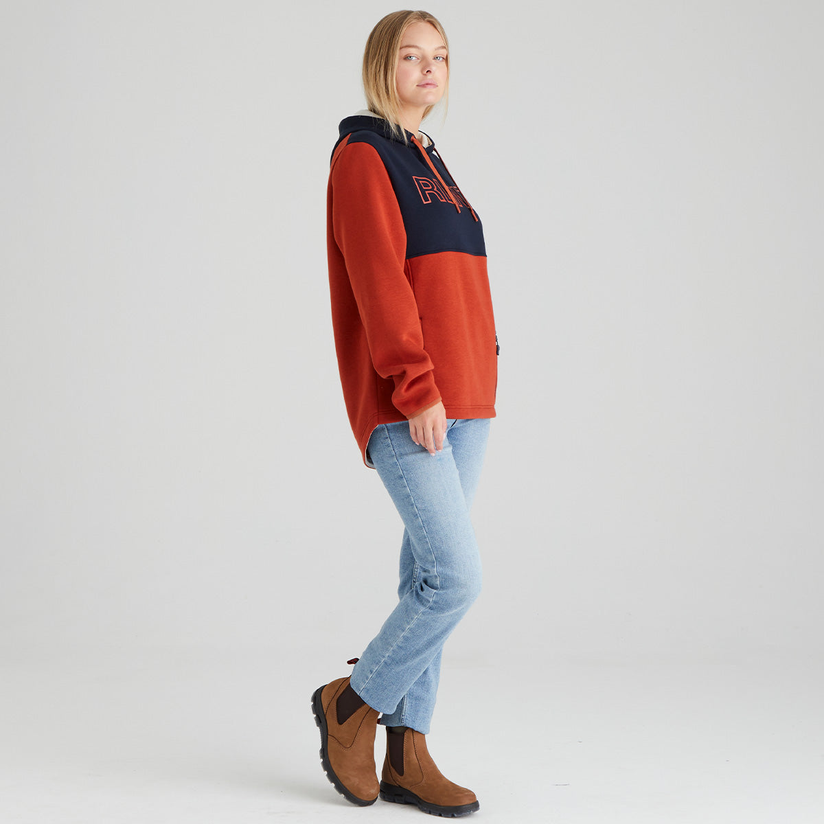 Person wearing a orange and navy hoodie with 'RLNZ' branding, light blue jeans, and brown boots on a white background.