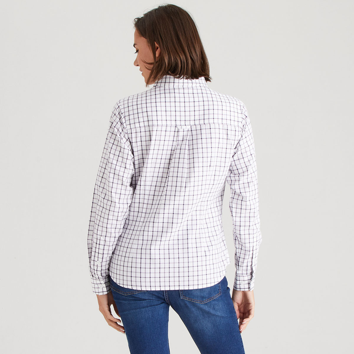 Woman wearing a white shirt with black checkered pattern and blue jeans on a light gray background