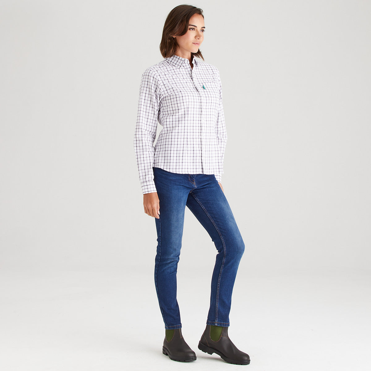 Woman wearing a checkered shirt, blue jeans, and black boots on a light gray background