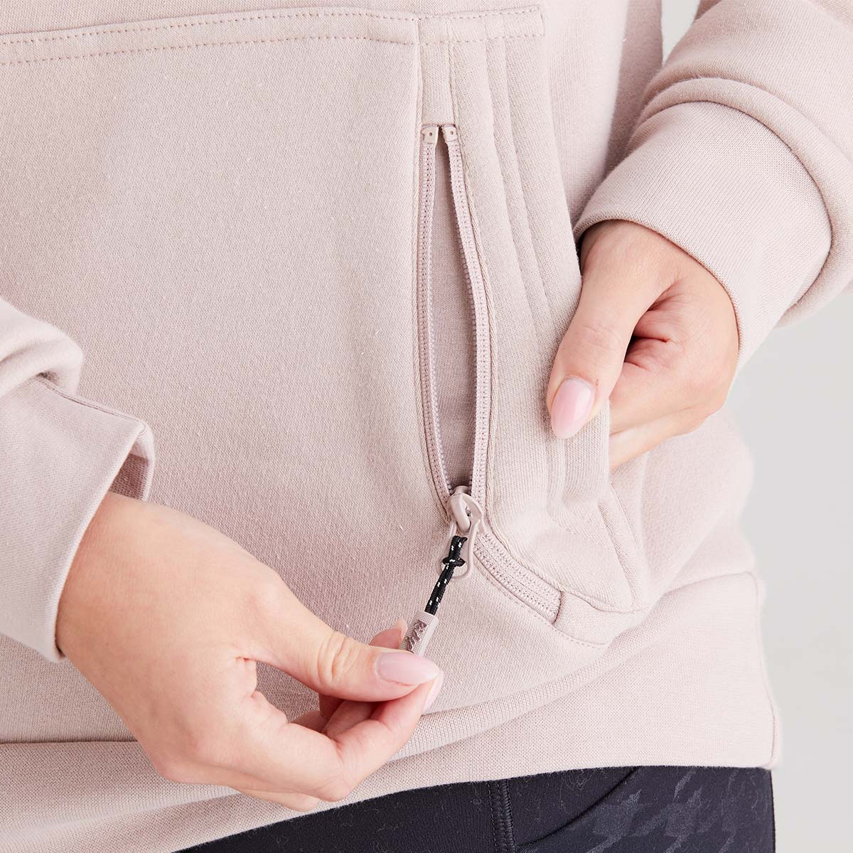 Person wearing a light pink hoodie with a zipper, focusing on the zipper mechanism.