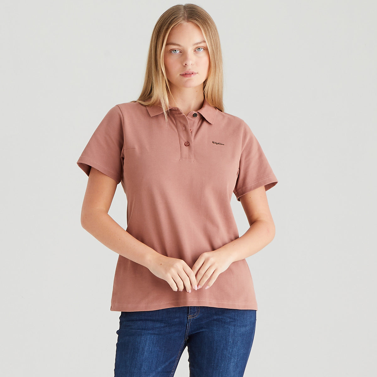 Woman wearing a pink polo shirt and blue jeans on a light gray background