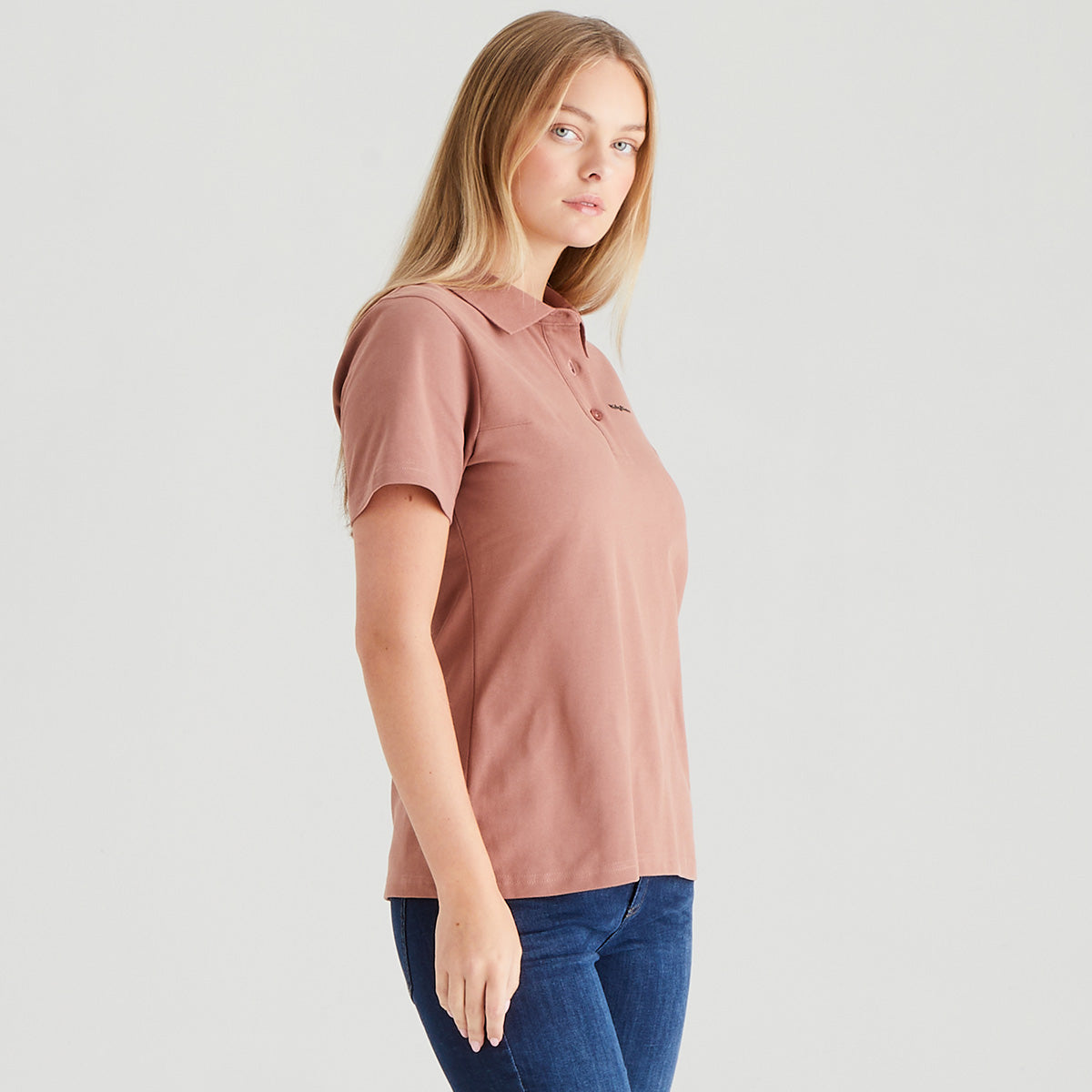 Woman wearing a pink polo shirt and blue jeans on a light gray background