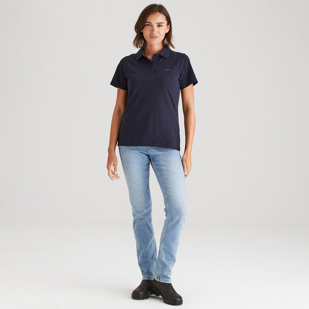 Woman wearing a navy polo shirt and light blue jeans on a white background