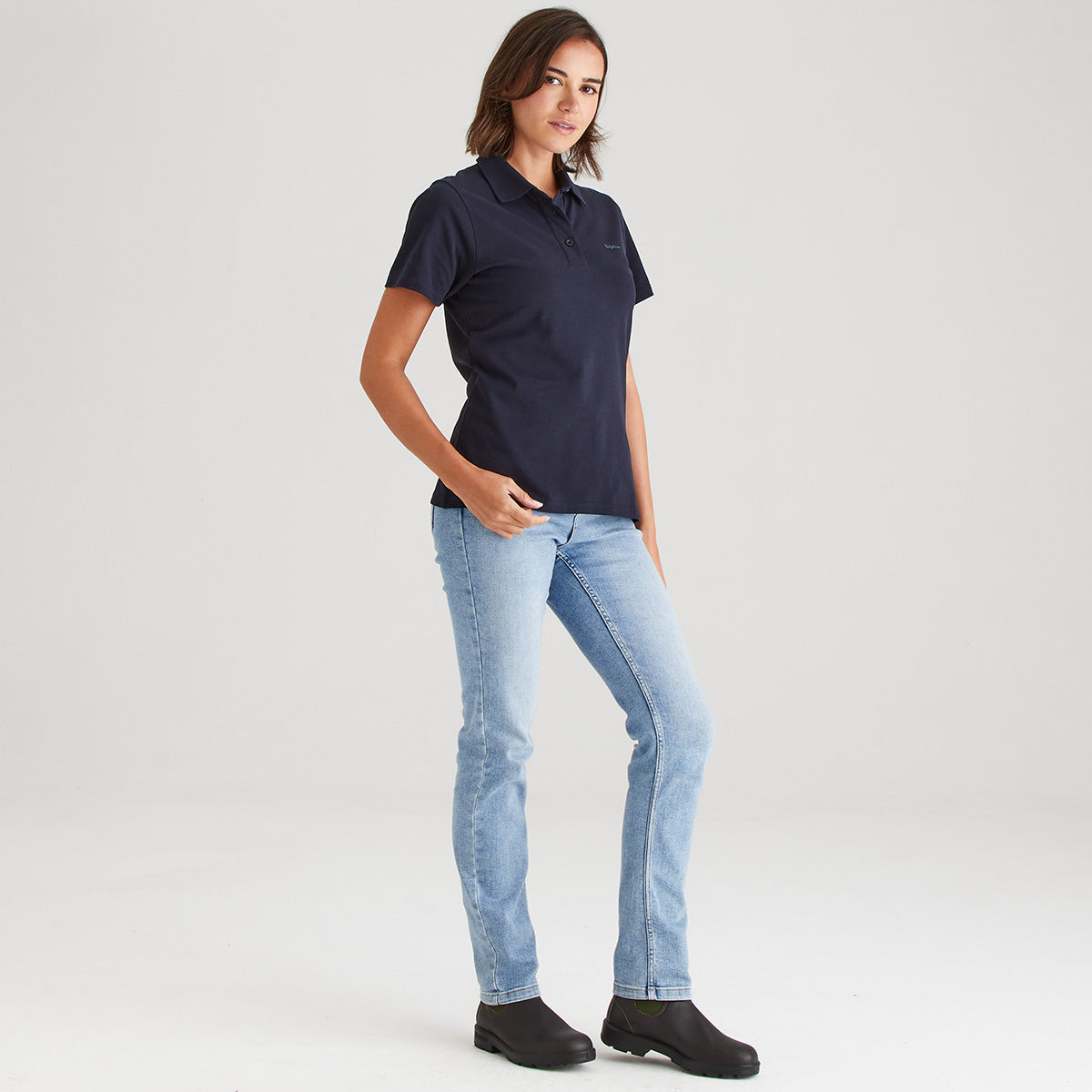 Person wearing a navy polo shirt and light blue jeans on a white background
