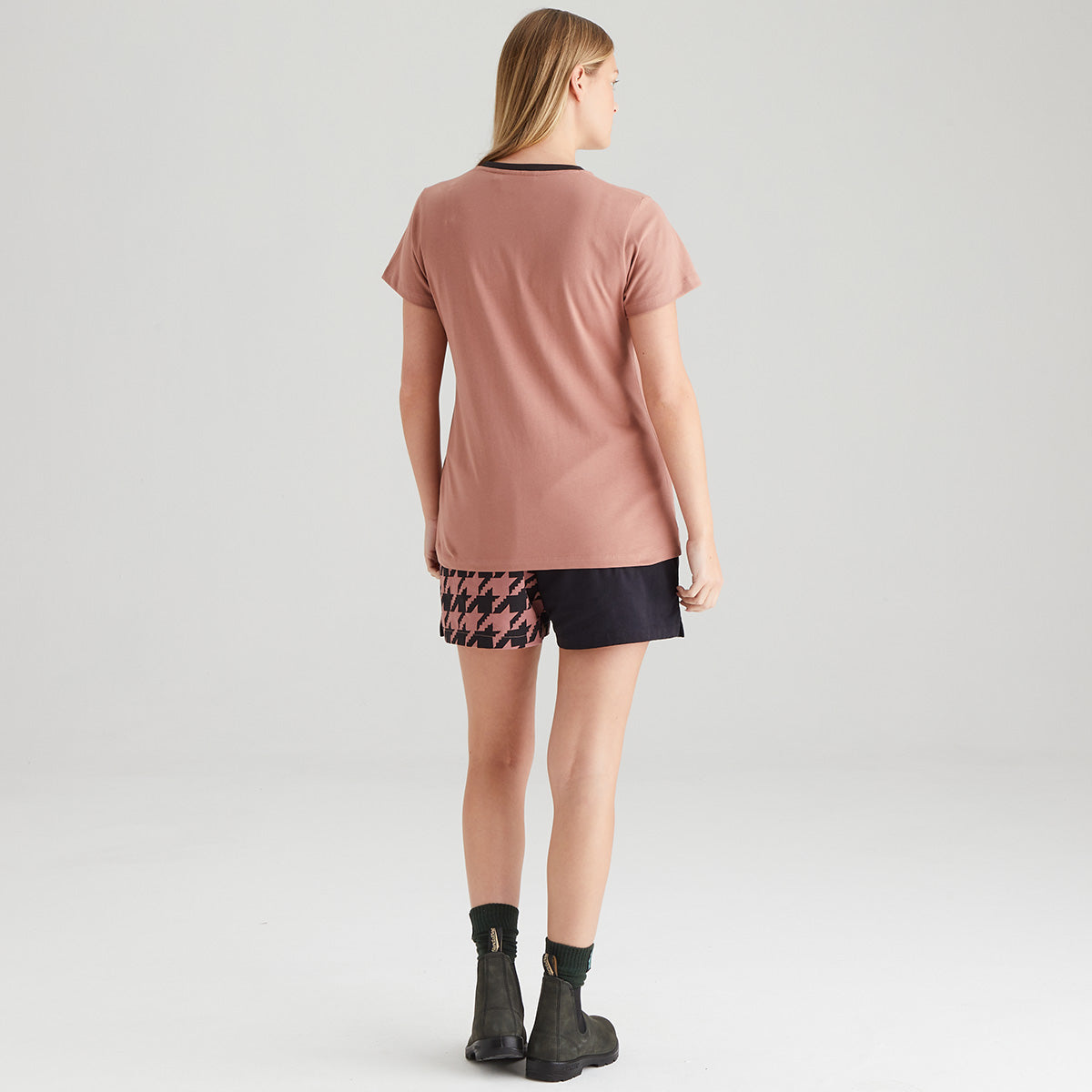 Person wearing a pink t-shirt and patterned shorts on a white background