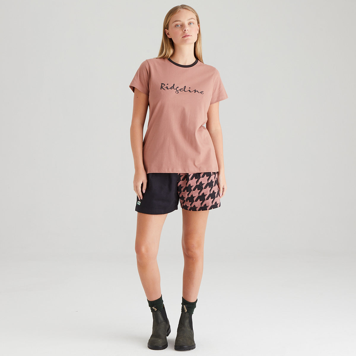 Woman wearing a pink t-shirt with 'Ridgeline' branding and patterned shorts on a white background