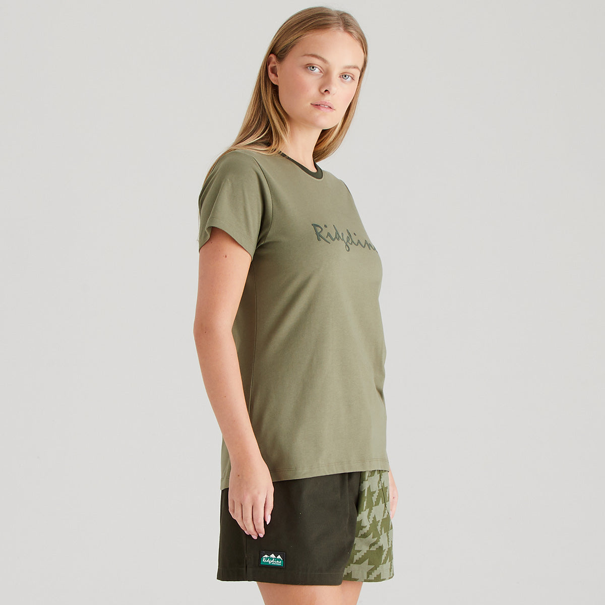 Woman wearing an olive green t-shirt with text on a plain background