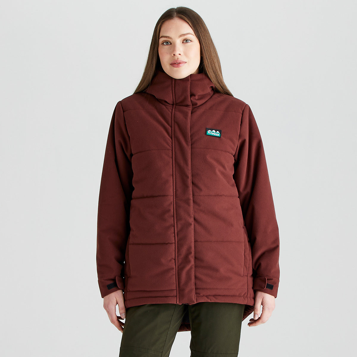 Person wearing a Ridgeline insulated jacket in burgundy with a full-length concealed zip, high collar, padded construction and adjustable cuffs, shown against a light grey studio background.
